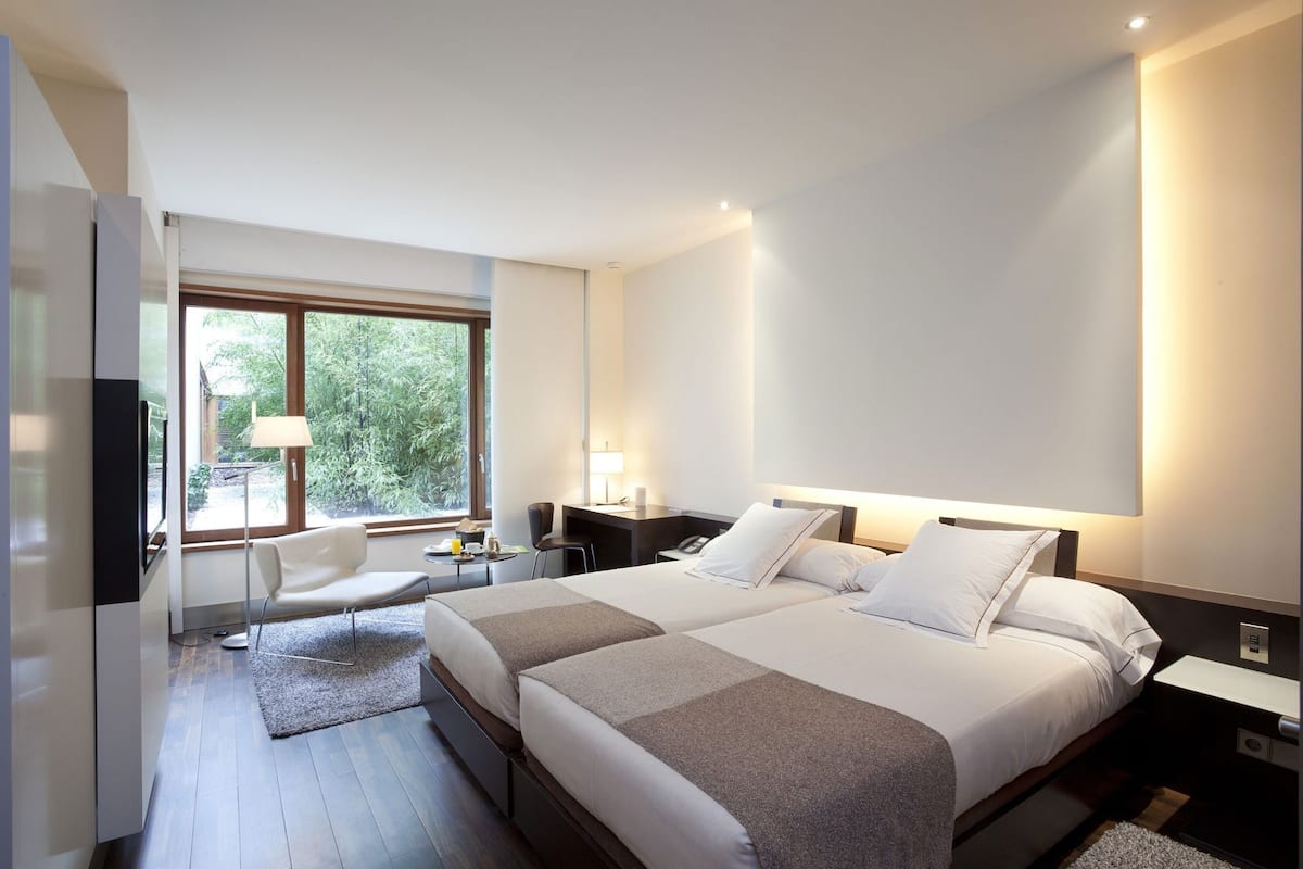 Une chambre d’hôtel moderne, dotée d’un grand lit, de tables de chevet, d’un bureau, d’une chaise et d’une fenêtre donnant sur un paysage verdoyant.