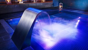 A modern spa area with a heated pool, a curved water feature, and candle-lit shelves. - Parador De Alcala (Alcala de Henares)