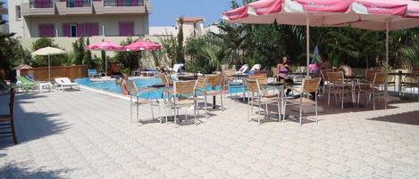 Ein Poolbereich mit Liegestühlen und Sonnenschirmen, ein Gebäude mit Balkonen und ein klarer Himmel.