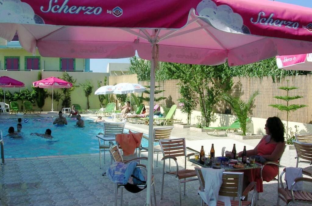A poolside area with lounge chairs, umbrellas, and a dining table with bottles.