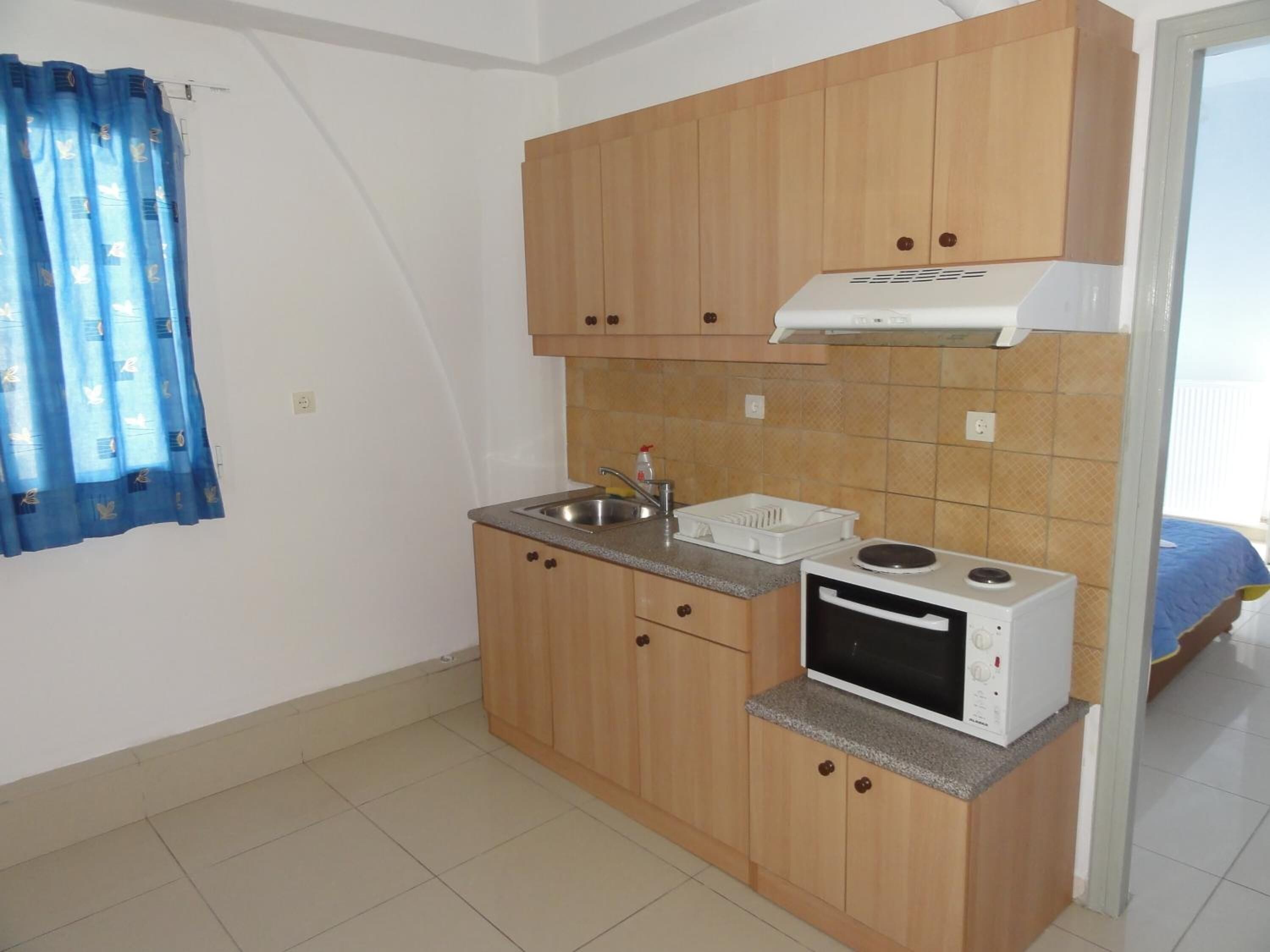 Una cocina compacta con armarios de madera, microondas integrado y un lavamanos.