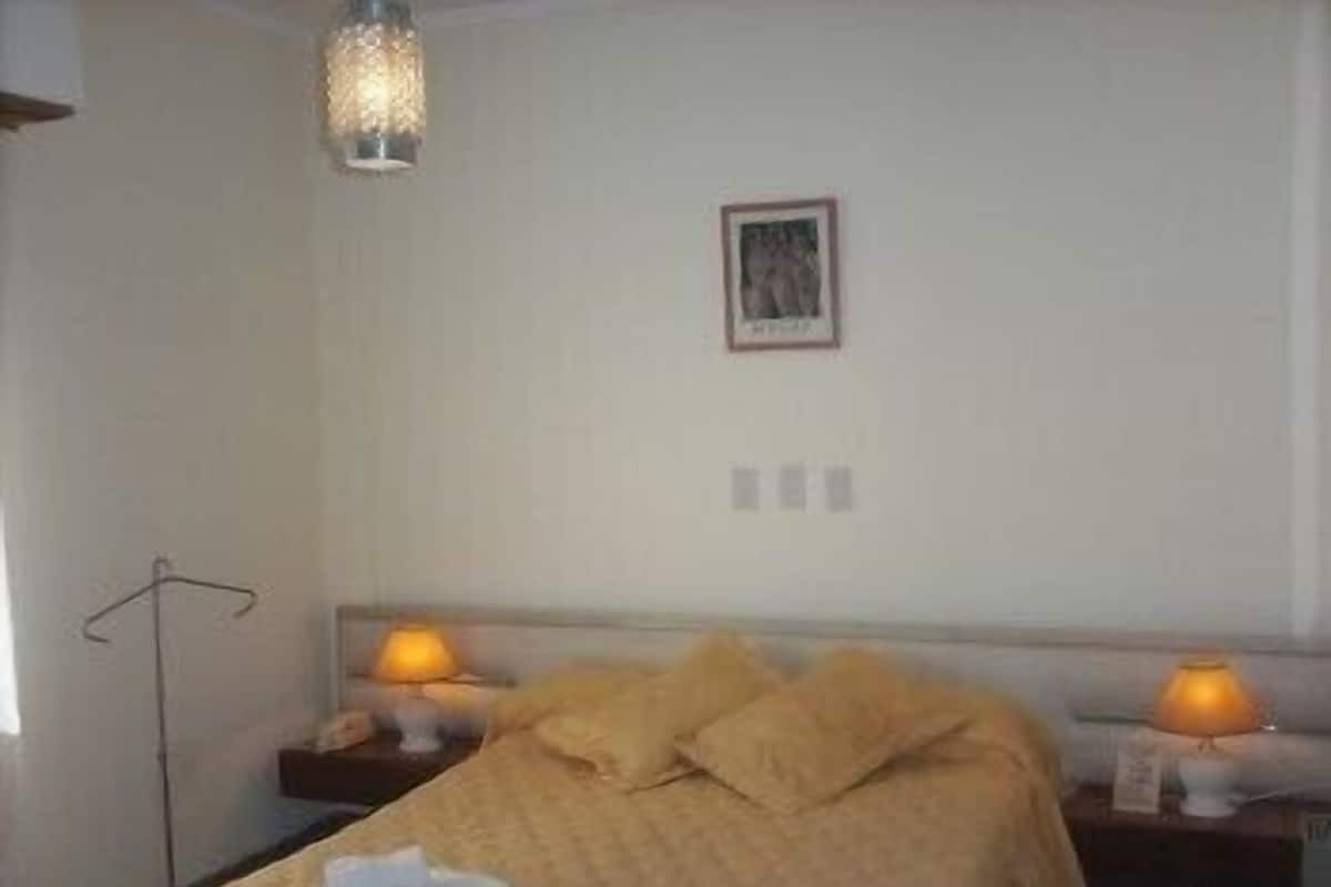 A bedroom with a bed, two bedside lamps, a hanging light fixture, and a framed picture on the wall.