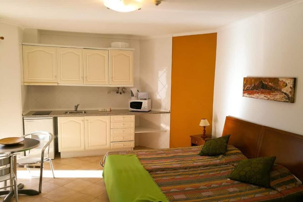 A compact room with a bed, a small kitchenette, and a dining area.