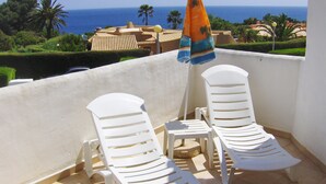 A balcony with two white lounge chairs and a small table, overlooking a scenic view of the ocean and palm trees. - Porto Mós Residence (Lagos)