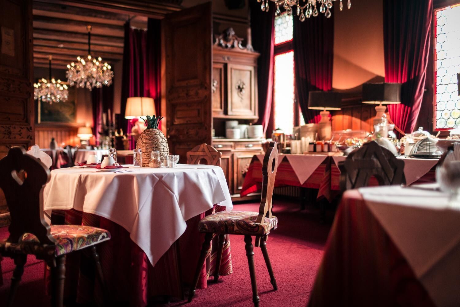 A restaurant with multiple tables, red curtains, and chandeliers.