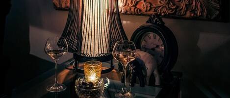 A table with a tall, ornate vase and two wine glasses, a candle, and a clock.