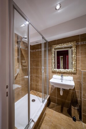 A bathroom with a glass shower enclosure, a sink with a mirror, and a trash bin. - Hotel Des Deux Clefs (Turckheim)