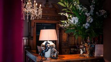 Una habitación con un escritorio de madera, una lámpara, un candelabro y un gran arreglo floral.