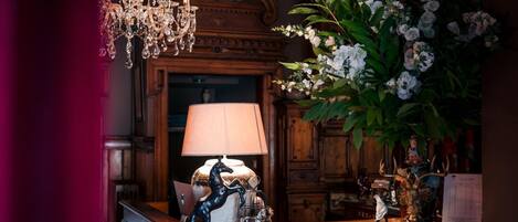 A room with a wooden desk, a lamp, a chandelier, and a large floral arrangement.