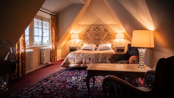 A cozy bedroom with a large bed, two bedside lamps, a wooden table, and a chair.