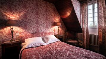 A bedroom with a sloped ceiling, floral wallpaper, a bed with a red and white patterned bedspread, two bedside lamps, and a radiator.