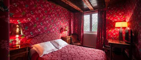 Una habitación con cama, mesita de noche, silla y ventana con cortinas.