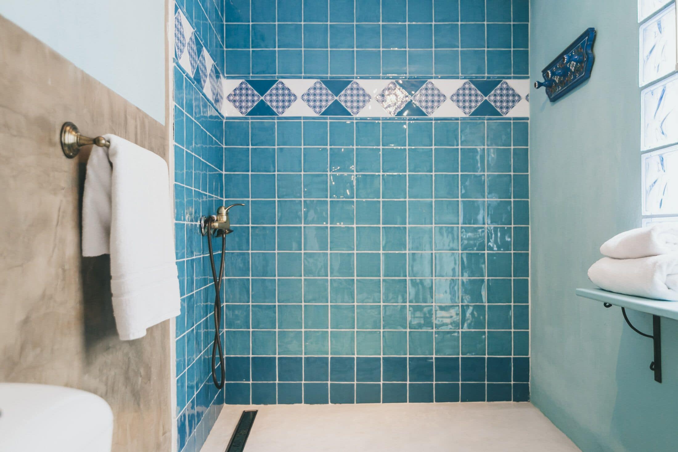 A bathroom with blue tiled walls, a shower, a toilet, and a sink with a towel rack.