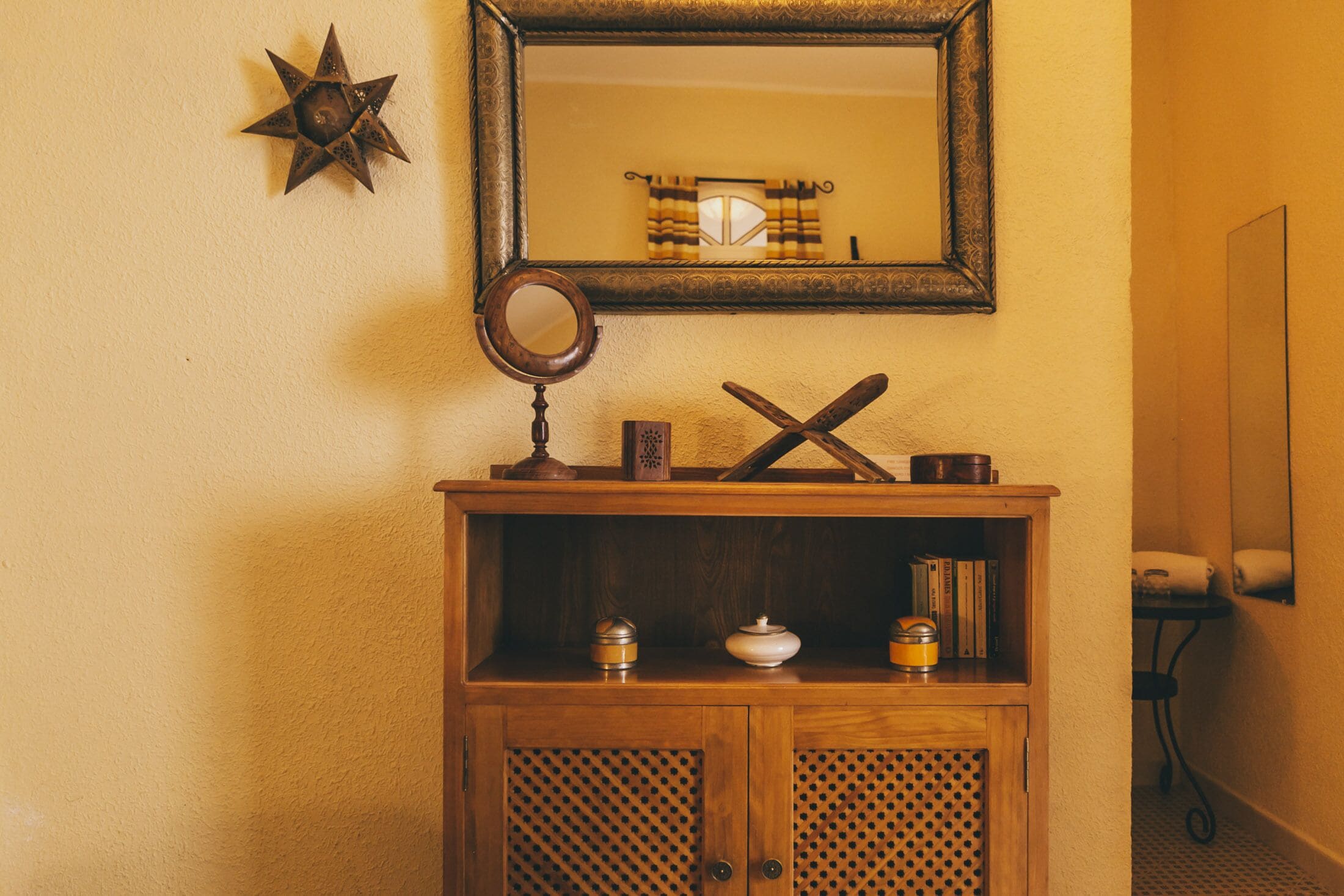Een houten kast met een spiegel erboven, een stersierad en een plank met boeken en bakken.