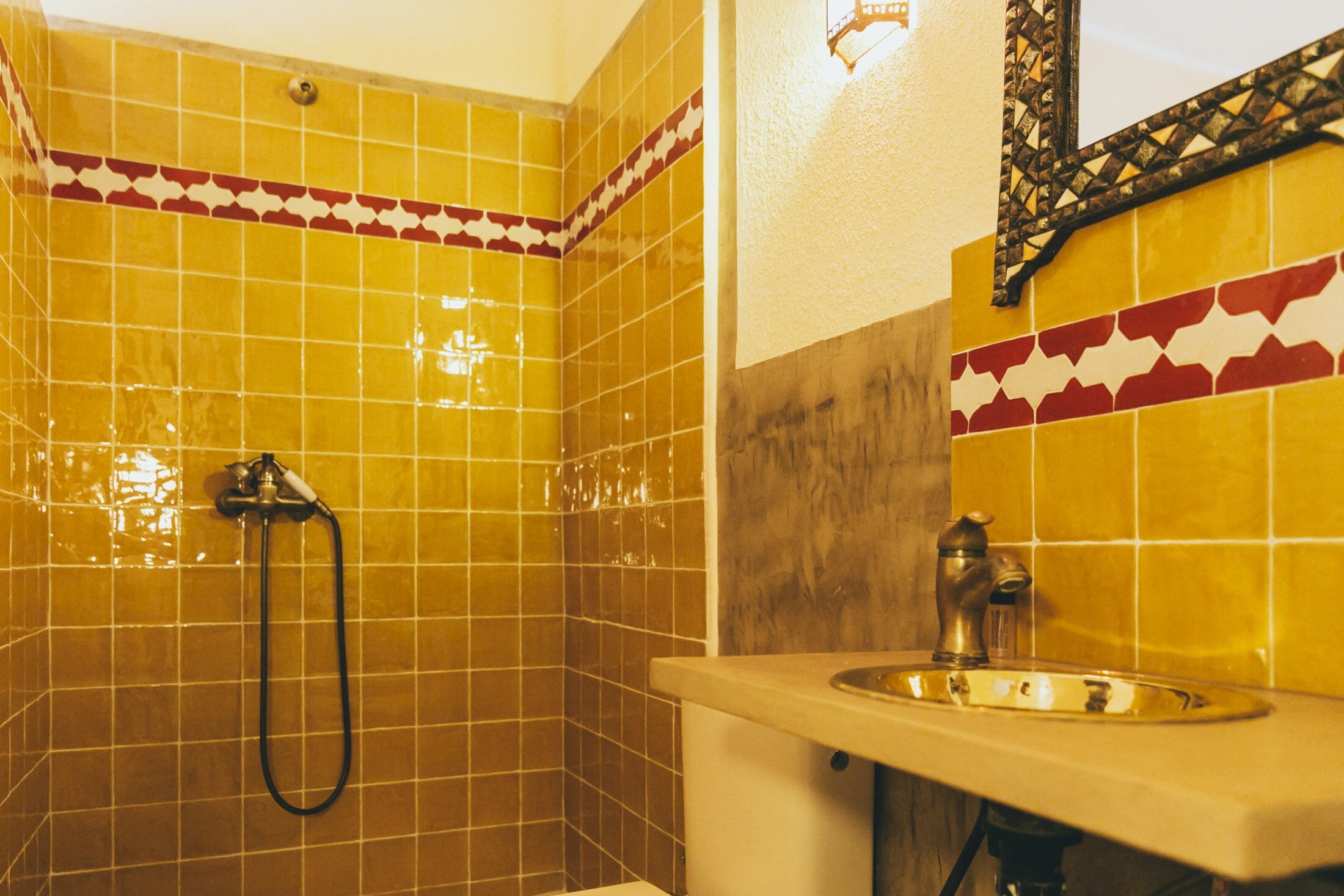 A bathroom with yellow tiled walls, a shower, and a sink with a mirror above it.
