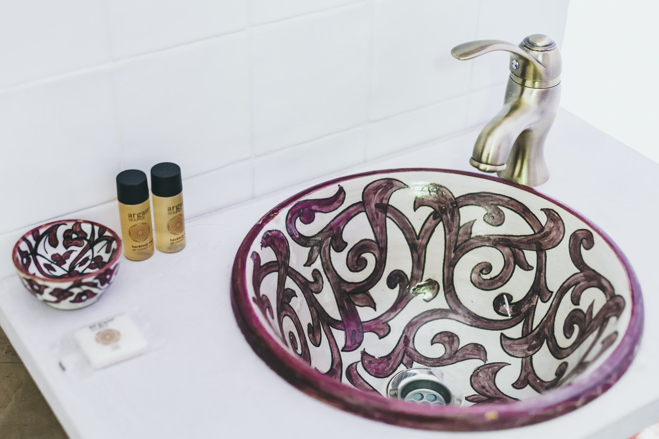 A bathroom sink with ornate designs, a modern faucet, and two toiletry bottles.