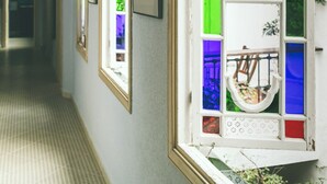 A hallway with a stained glass window, framed pictures on the wall, and a patterned floor. - EL Riad Andaluz - Guest House (Málaga)
