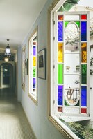 Un pasillo con un ventanal de vitrales, cuadros enmarcados en la pared y un suelo con diseño.