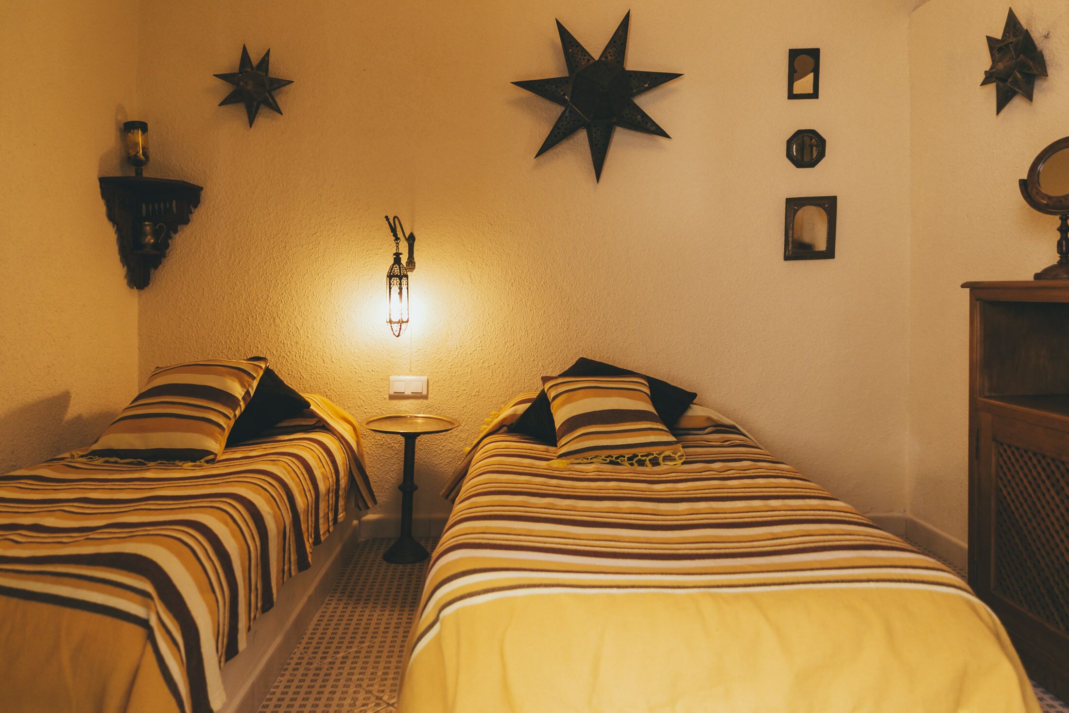 A room with two beds, a wall-mounted star decoration, and a small table with a lamp.