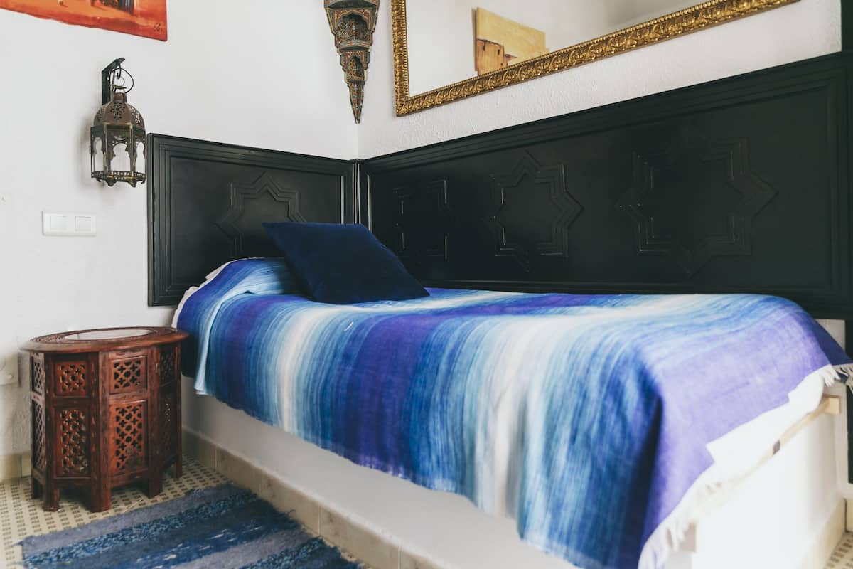 A bed with a blue and white striped blanket, a dark headboard, a small wooden side table, and a wall-mounted lantern.