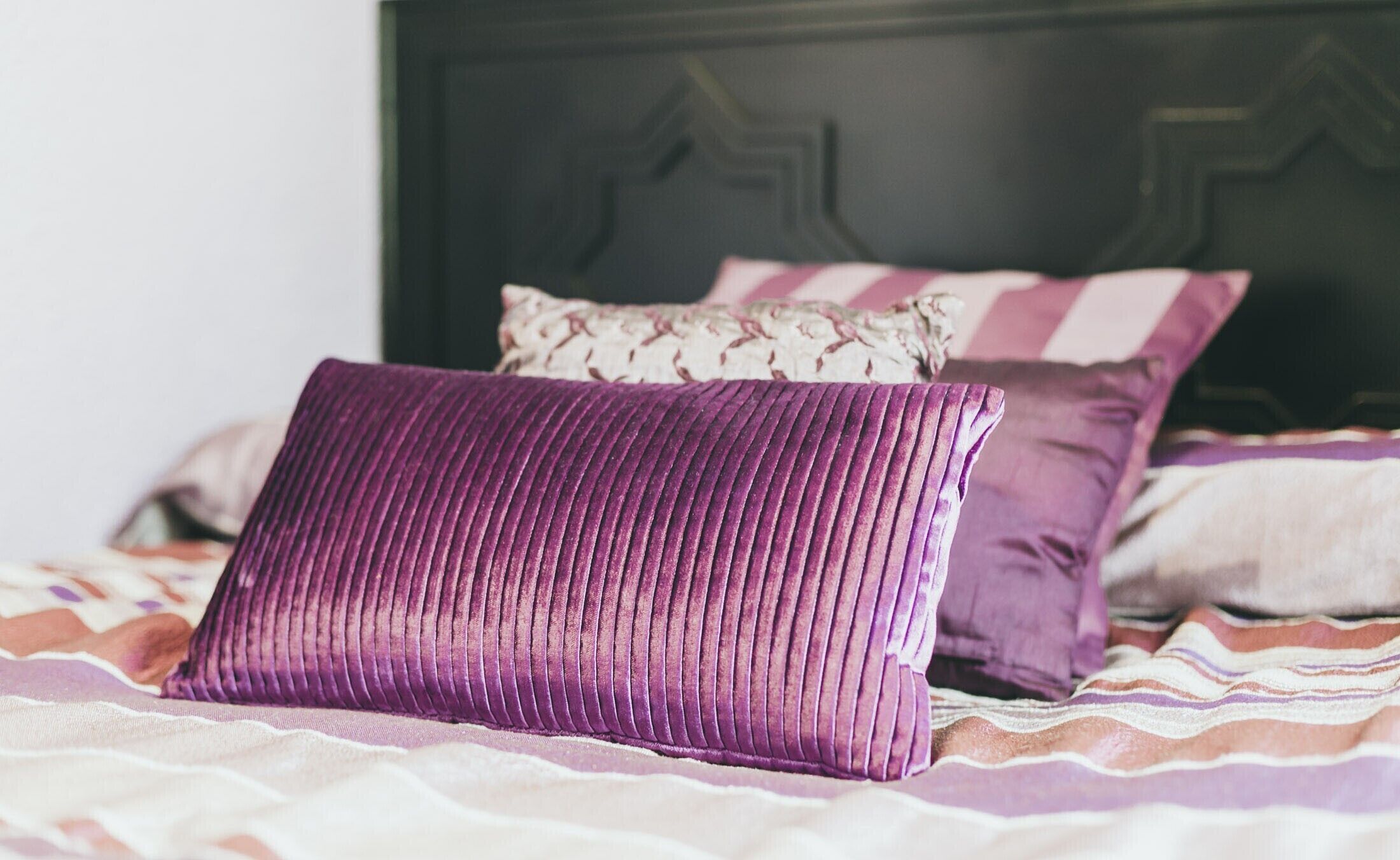 Una cama con un almohadón morado y una almohada a rayas.
