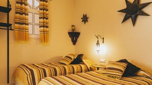 A room with two beds, striped bedding, a star-shaped wall decoration, a wall-mounted light fixture, and a window with curtains. - EL Riad Andaluz - Guest House (Málaga)