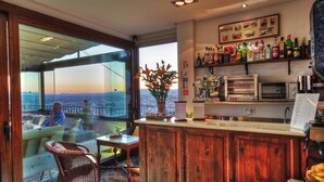 A bar area with a view of the city, a wicker chair, a table with a vase of flowers, and a variety of liquor bottles. - Hotel Mirador Arabeluj (Granada)