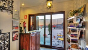 A room with a wooden cabinet, a glass door leading to an outdoor area with potted plants and a chair, and a shelf with various items. - Hotel Mirador Arabeluj (Granada)