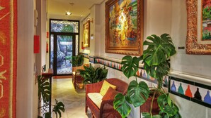 A hallway with a wicker sofa, large potted plants, and a painting on the wall. - Hotel Mirador Arabeluj (Granada)