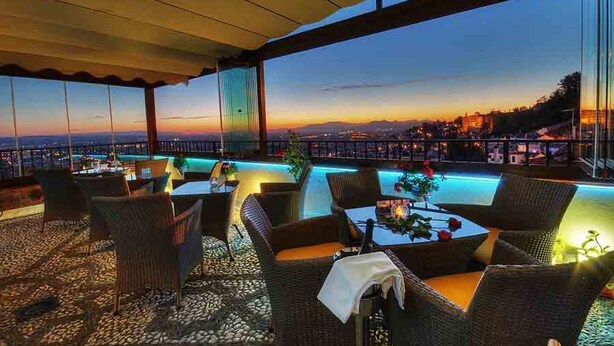 An outdoor seating area with wicker furniture and a pool, overlooking a cityscape at dusk. - Hotel Mirador Arabeluj (Granada)