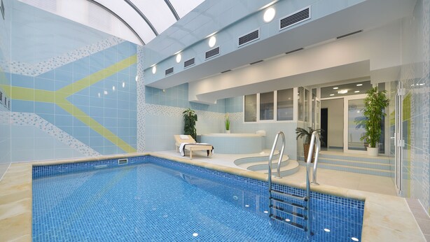 Une piscine intérieure avec un sol carrelé, une échelle et un espace détente comprenant un banc et des plantes en pot.