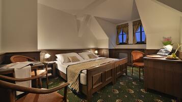 A hotel room with a wooden bed, a desk with a lamp, a chair, and a window with curtains.