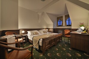 A hotel room with a wooden bed, a desk with a lamp, a chair, and a window with curtains.
