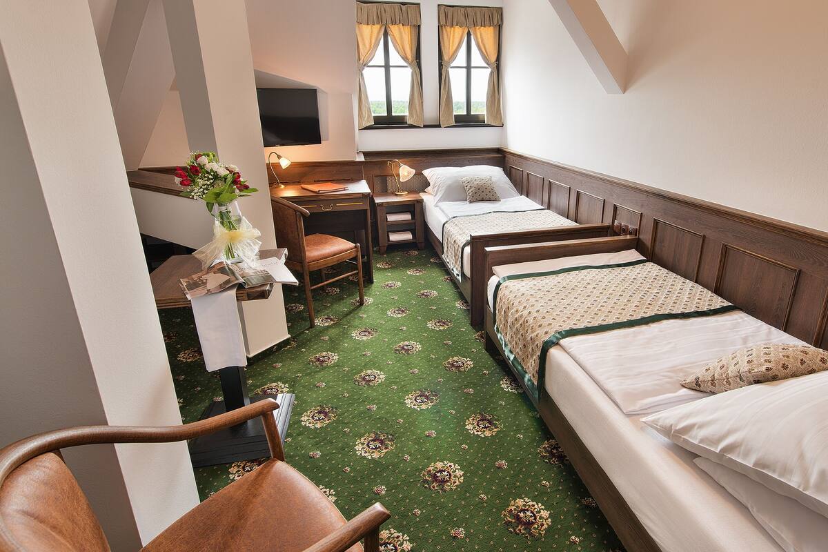 Ein Hotelzimmer mit zwei Einzelbetten, einem Schreibtisch mit Stuhl, einem Fernseher und einem Fenster mit Vorhängen.