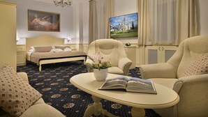 Une chambre d’hôtel avec un lit, deux fauteuils, une petite table avec un livre et des fleurs, un tableau au mur et un téléviseur.