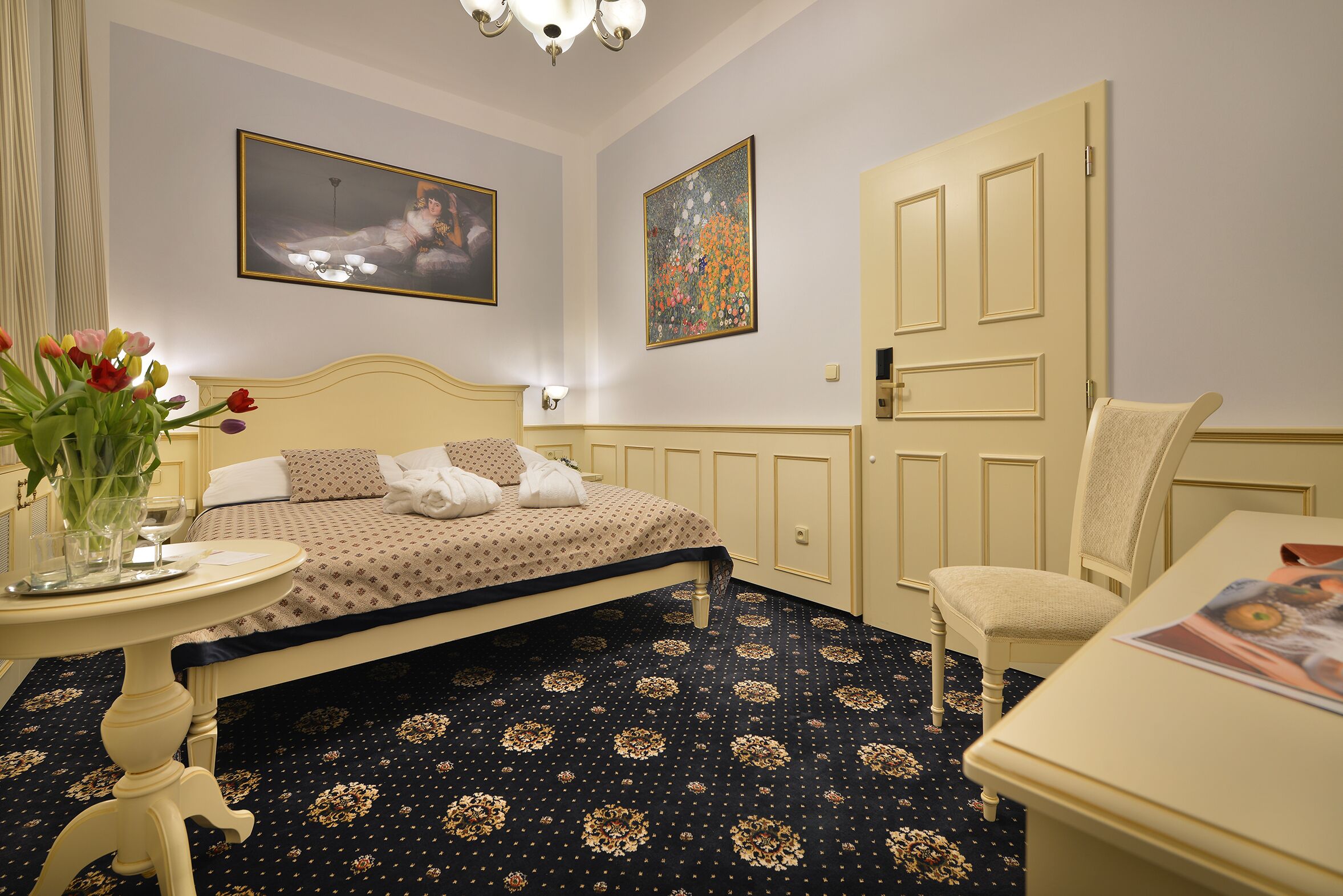 Habitación de hotel con cama, una silla, una mesa y un jarrón de flores.