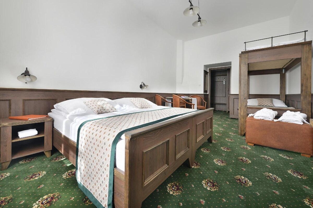 Une chambre d’hôtel avec un lit en bois, une table de chevet, une armoire et un tapis à motifs verts.