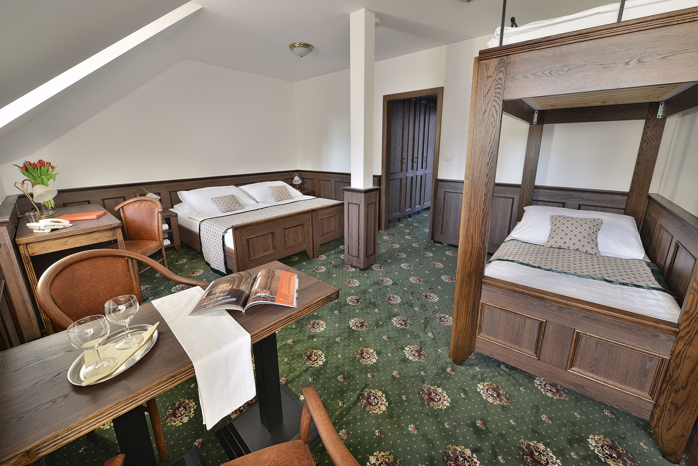 A room with a bunk bed, a desk with a chair, a dining table with a tray of wine glasses, and a book.