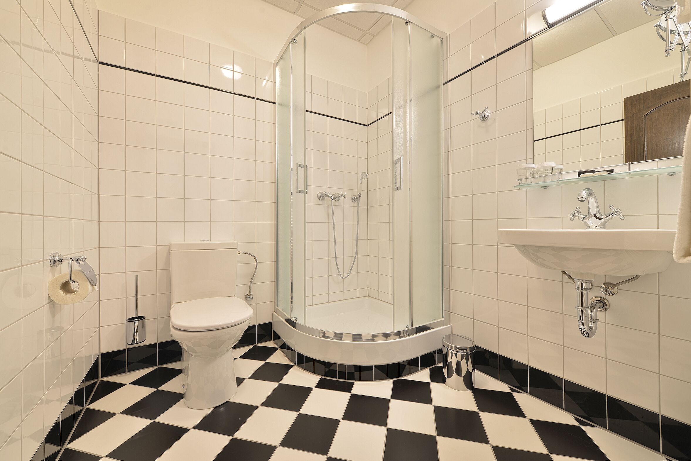 A bathroom with a glass-enclosed shower, a toilet, and a sink with a mirror above it.