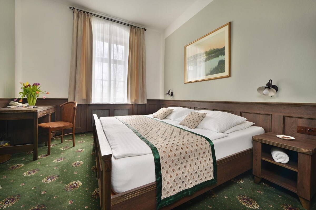 Une chambre d’hôtel avec un lit, un bureau, une chaise, une table de chevet, une lampe et un tableau au mur.