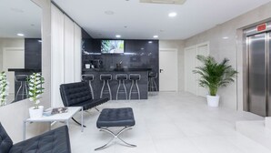 A modern kitchen with dark countertops and a flat-screen TV. There are bar stools and a black sofa in the dining area. - Di Carlo Hotels Madrid (Madrid)