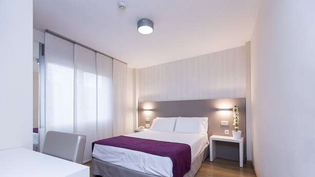 A modern hotel room with a bed, bedside table, and a desk with a chair. - Di Carlo Hotels Madrid (Madrid)