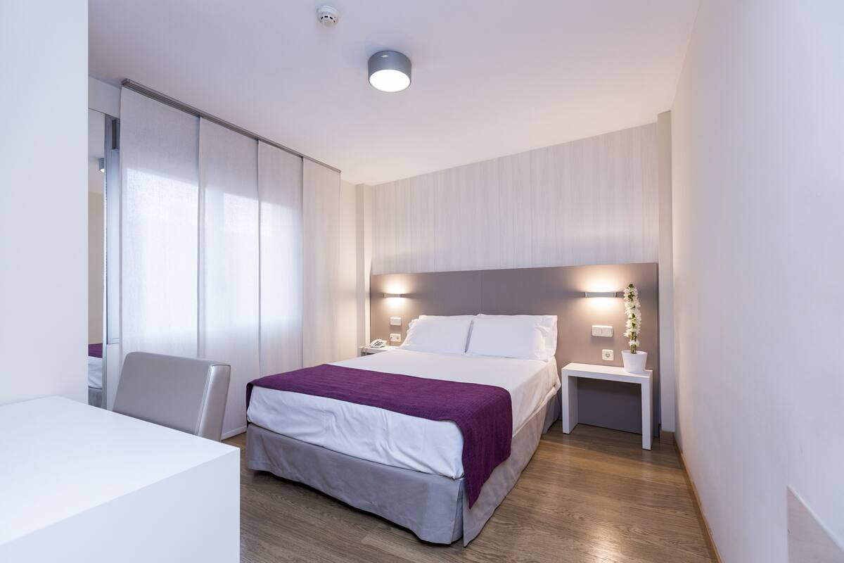 Une chambre d’hôtel moderne équipée d’un lit, d’une table de chevet et d’un bureau avec une chaise.