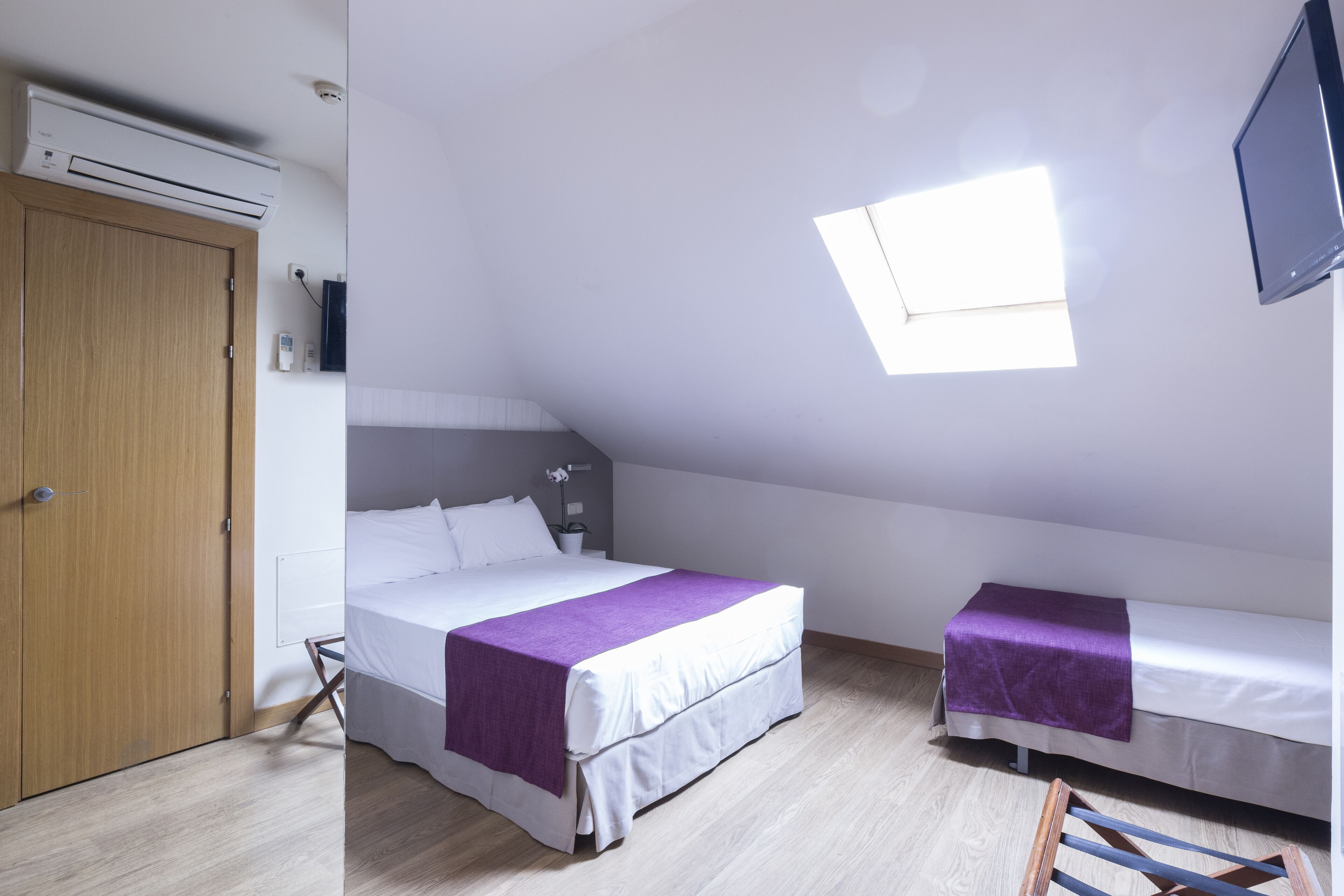 Un dormitorio con una cama grande, una cama más pequeña, un televisor, una ventana y un armario.