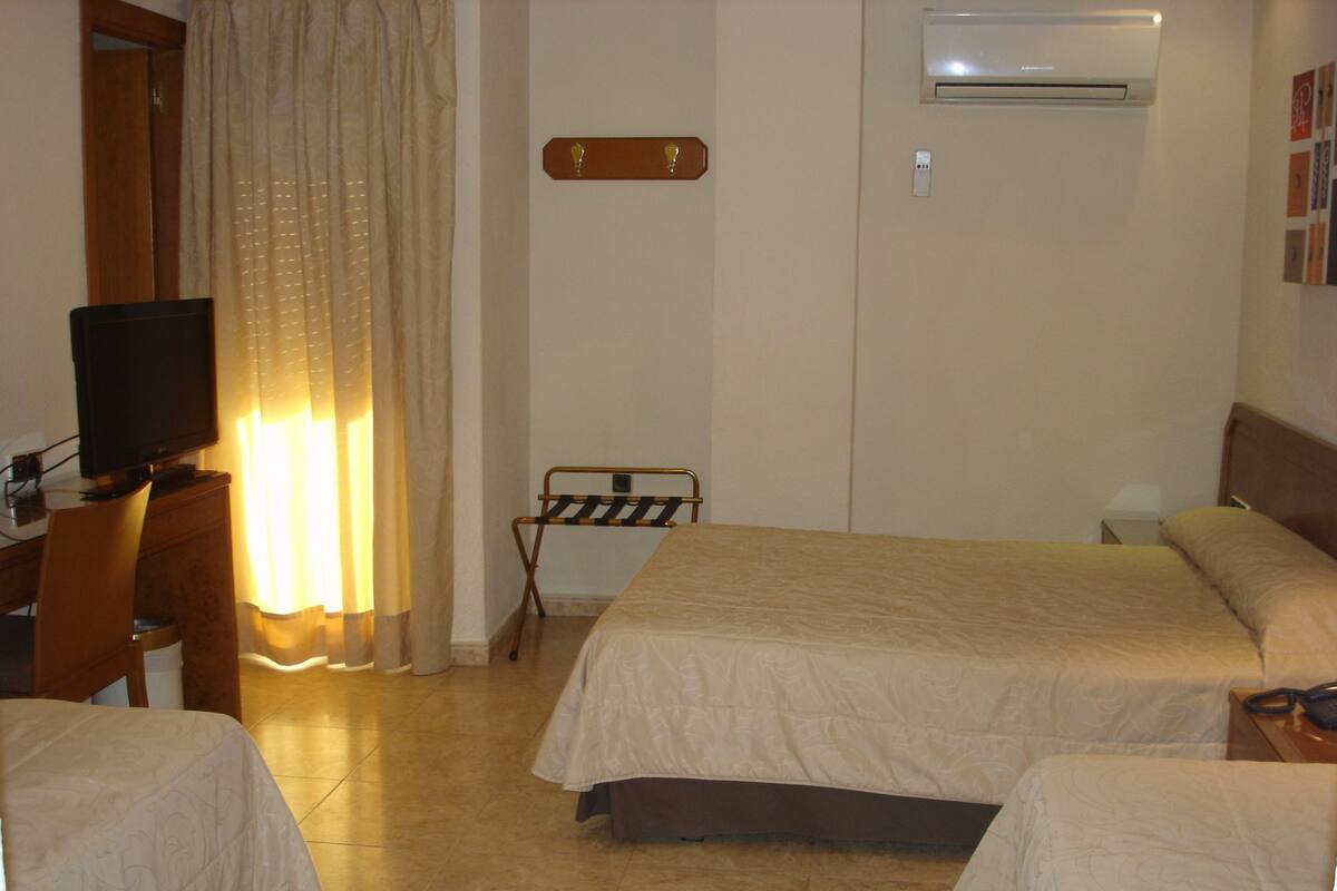 Habitación de hotel con dos camas, un televisor, un tendedero y un equipo de aire acondicionado.