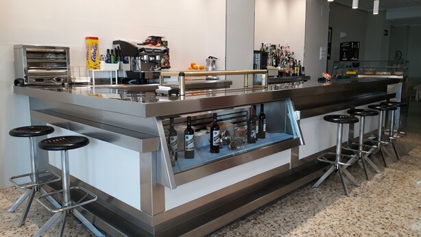 Eine moderne Bar mit Edelstahl-Theken, Barhocker und einer Auswahl an Flaschen.