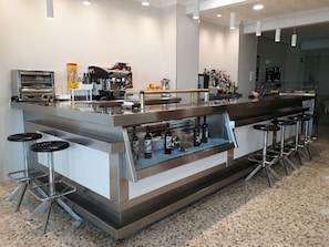 Zona de bar moderna con mostradores de acero inoxidable, taburetes y una variedad de botellas.