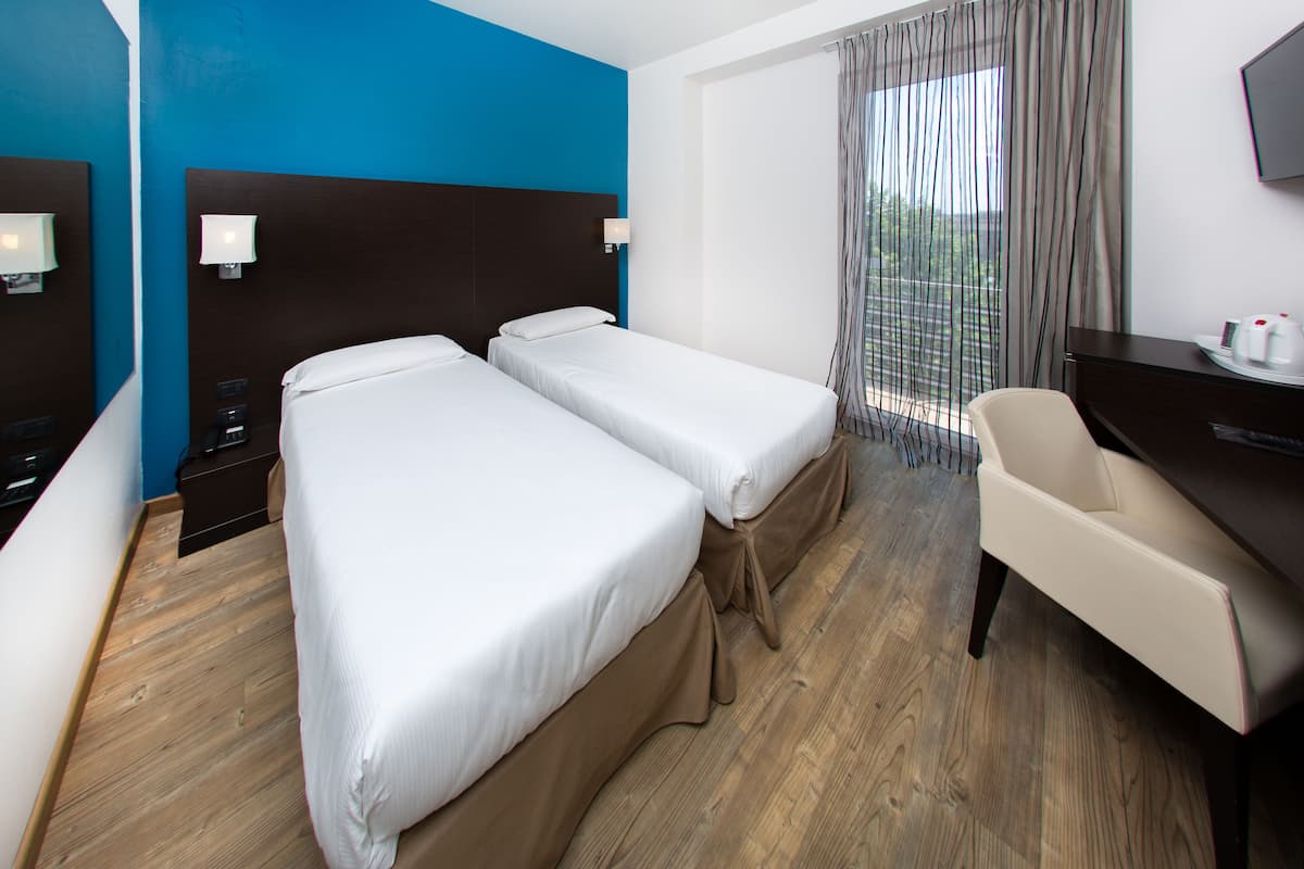 Une chambre d’hôtel avec deux lits, un bureau, une chaise et un téléviseur fixé au mur.
