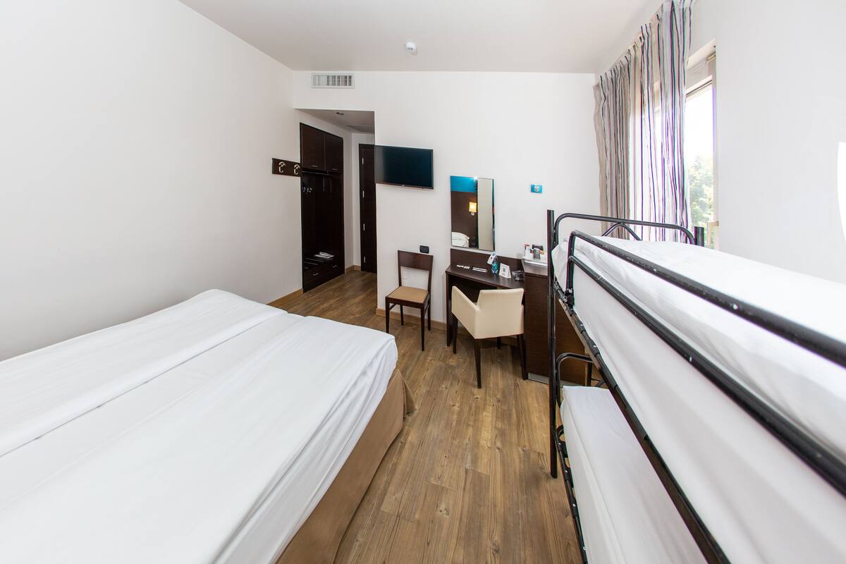Une chambre d’hôtel avec deux lits simples, un bureau avec une chaise, un miroir et une télévision.