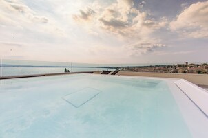 Una piscina infinita en la azotea con vista despejada al mar y un paisaje urbano distante.